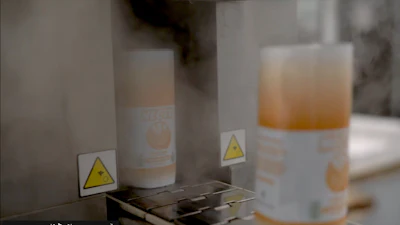 Bottles with applied shrink sleeves enter a steam tunnel to shrink labels around the bottles.