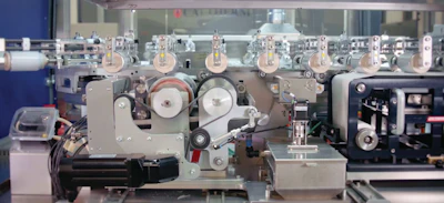 On this oval-shaped track are multiple paired tools. Each pair grips one can from opposite sides and carries it first past a belt that wipes down each can surface. Then each can is rotated against a roller coater for application of a proprietary toner. Only then are cans ready for digital printing.