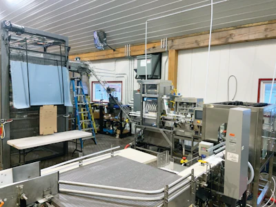 A wide view of the canning line, with cans being conveyed from depalletizer in the upper left to a canner and seaming station in the upper middle. A can dryer and checkweigher are on the right, and cans enter accumulation in the foreground before tray packing downstream.