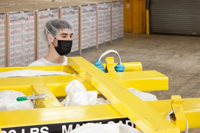 At floor level, an operator attaches bulk bag straps to Z-Clip strap holders of a bag lifting frame held in position by a forklift.