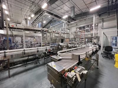 In this wide-angle photo of the packaging line, we can see an accumulation table ahead of a PakTech can handle applicator, Bevco conveyance, and a DMM case/tray packing in the background.