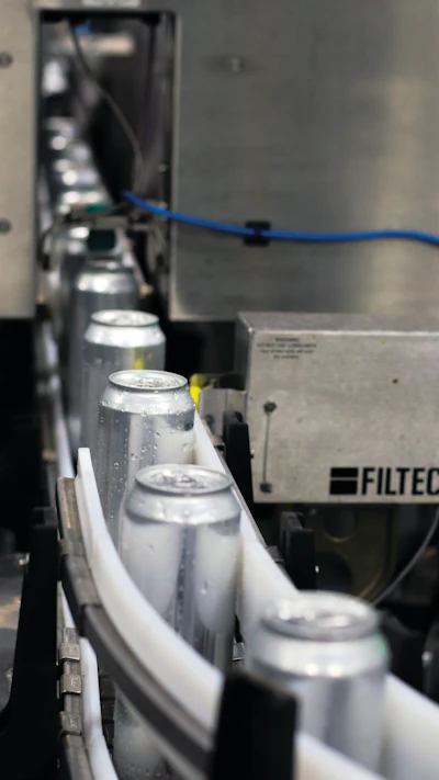 Filled and seamed bright stock cans get a Filtec fill-level check prior to date coding and labeling.