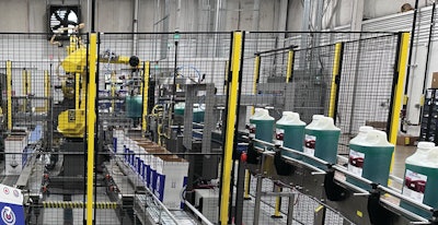 Here, secondary packaging operations begin. The lines of erected cases with partition that exit the box shop (left) are joined with the lines of filled, labeled and capped bottles, for robotic case packing.