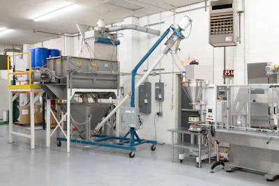 The ribbon blender is fed through a bag dump station and discharges to a floor hopper before blending.