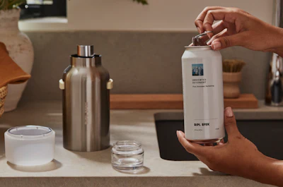 The aluminum refill can is opened and inserted into the reusable stainless steel vessel, where it locks into place for dispensing.